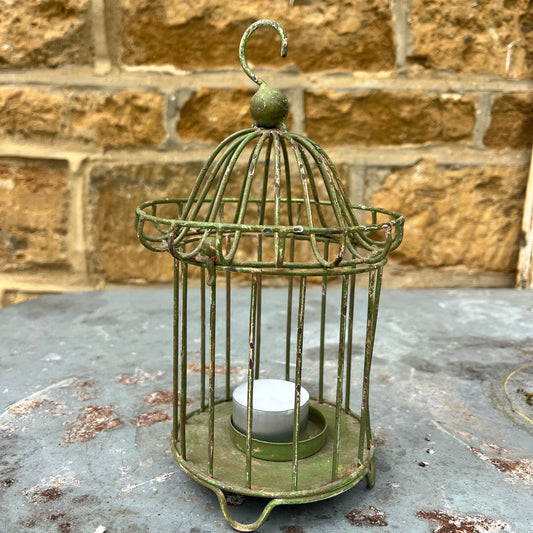 Green metal birdcage with a candle inside on a metal surface