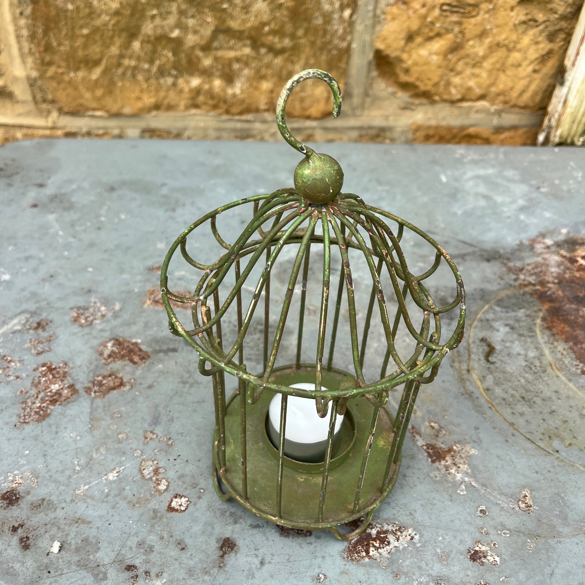 Green metal birdcage with a candle inside on a metal surface