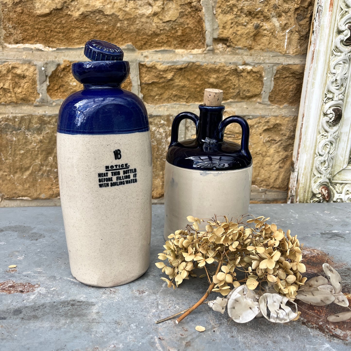 A stoneware flagon with a robust, earthy brown base transitioning to a glossy blue glaze on the top half. The flagon features two sturdy handles and a narrow stoppered spout, exuding rustic charm. also a hot water vessel with the same colouring.