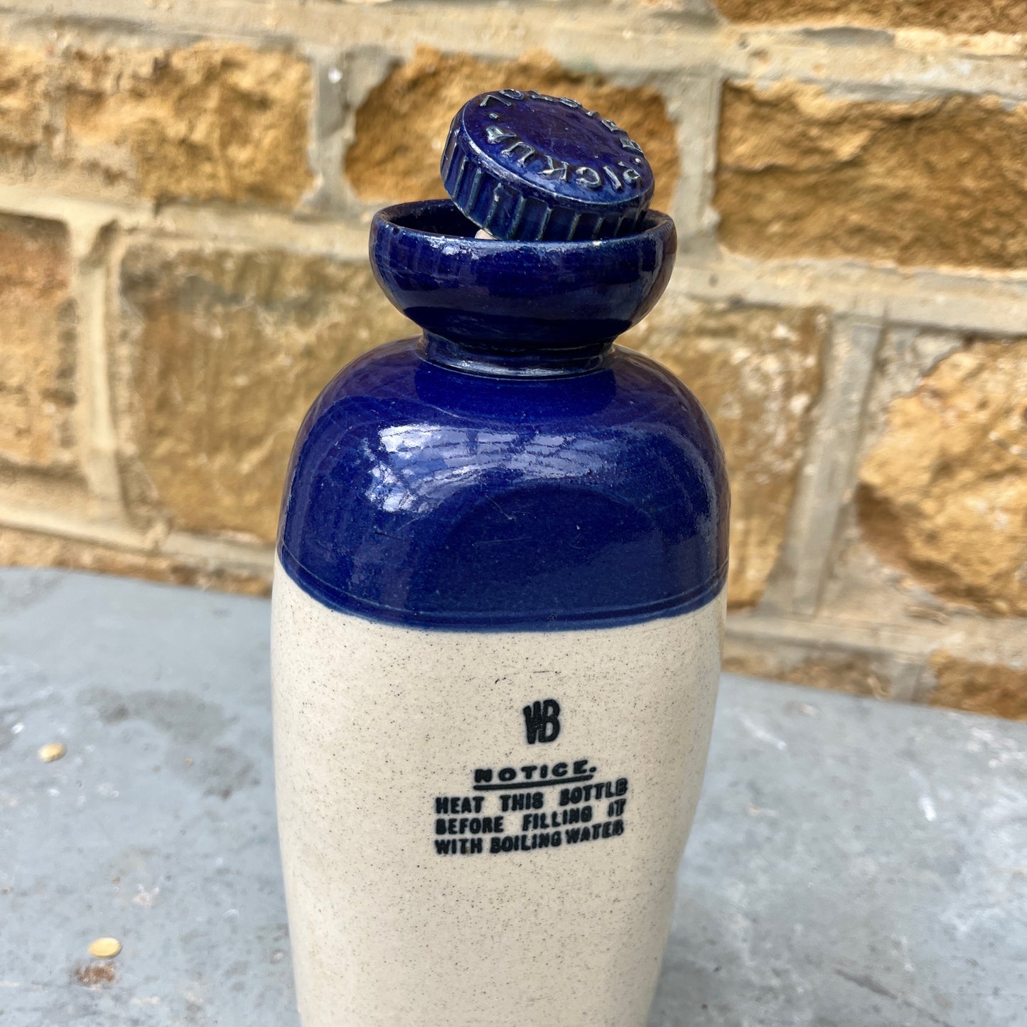 A stoneware flagon with a robust, earthy brown base transitioning to a glossy blue glaze on the top half. The flagon features two sturdy handles and a narrow stoppered spout, exuding rustic charm. Also a hot water vessel with the same colouring