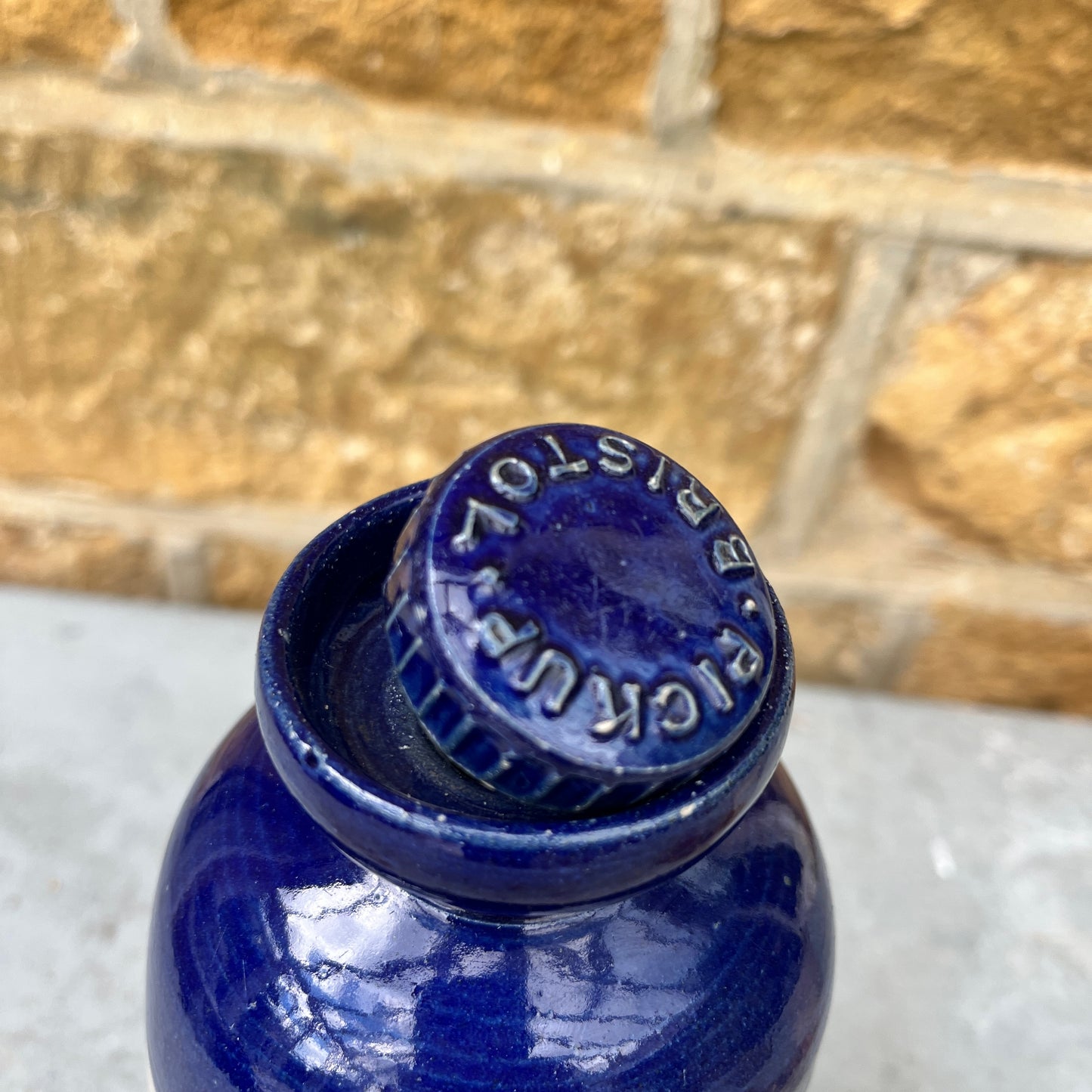 A stoneware flagon with a robust, earthy brown base transitioning to a glossy blue glaze on the top half. The flagon features two sturdy handles and a narrow stoppered spout, exuding rustic charm. Also a hot water vessel with the same colouring