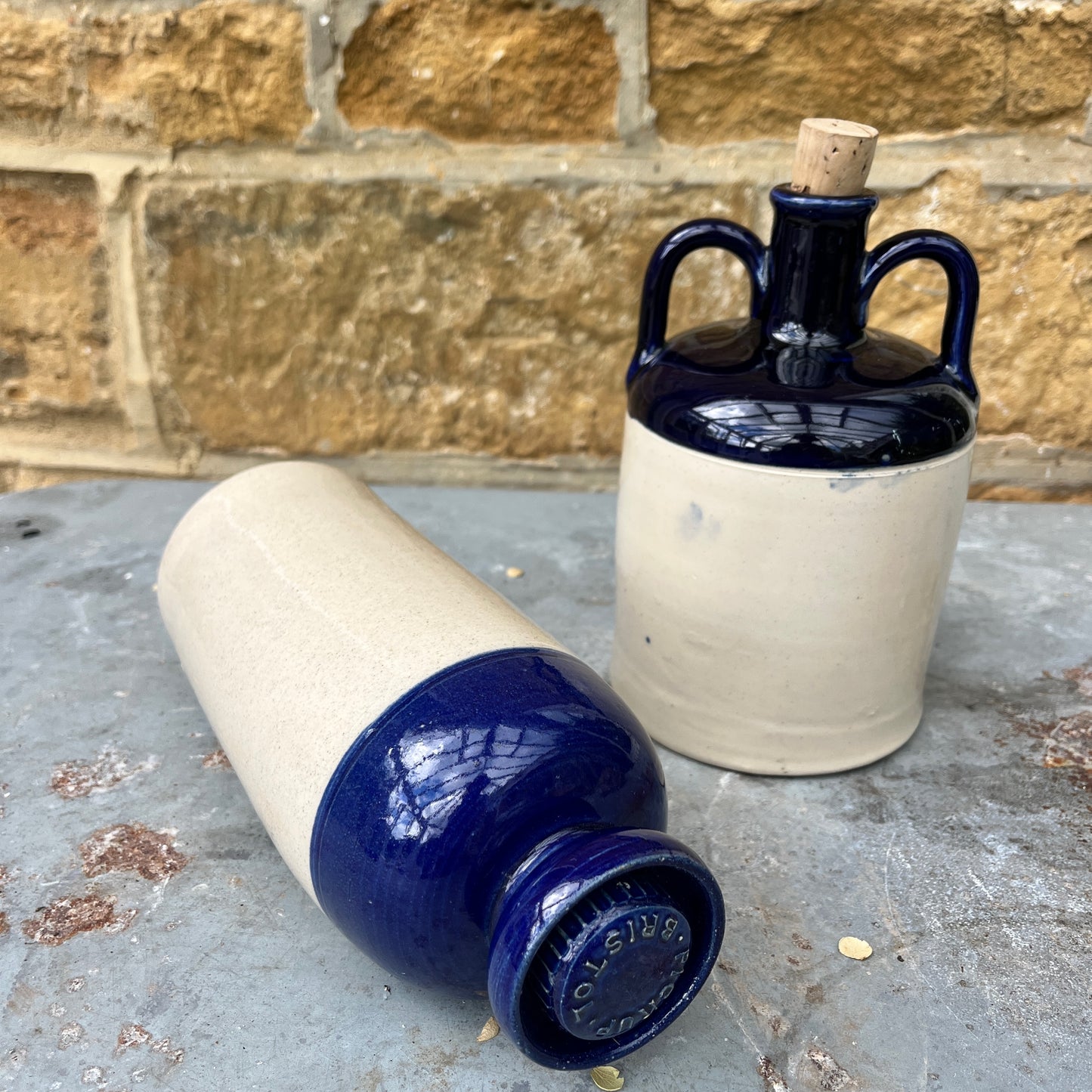 A stoneware flagon with a robust, earthy brown base transitioning to a glossy blue glaze on the top half. The flagon features two sturdy handles and a narrow stoppered spout, exuding rustic charm. Also a hot water vessel with the same colouring