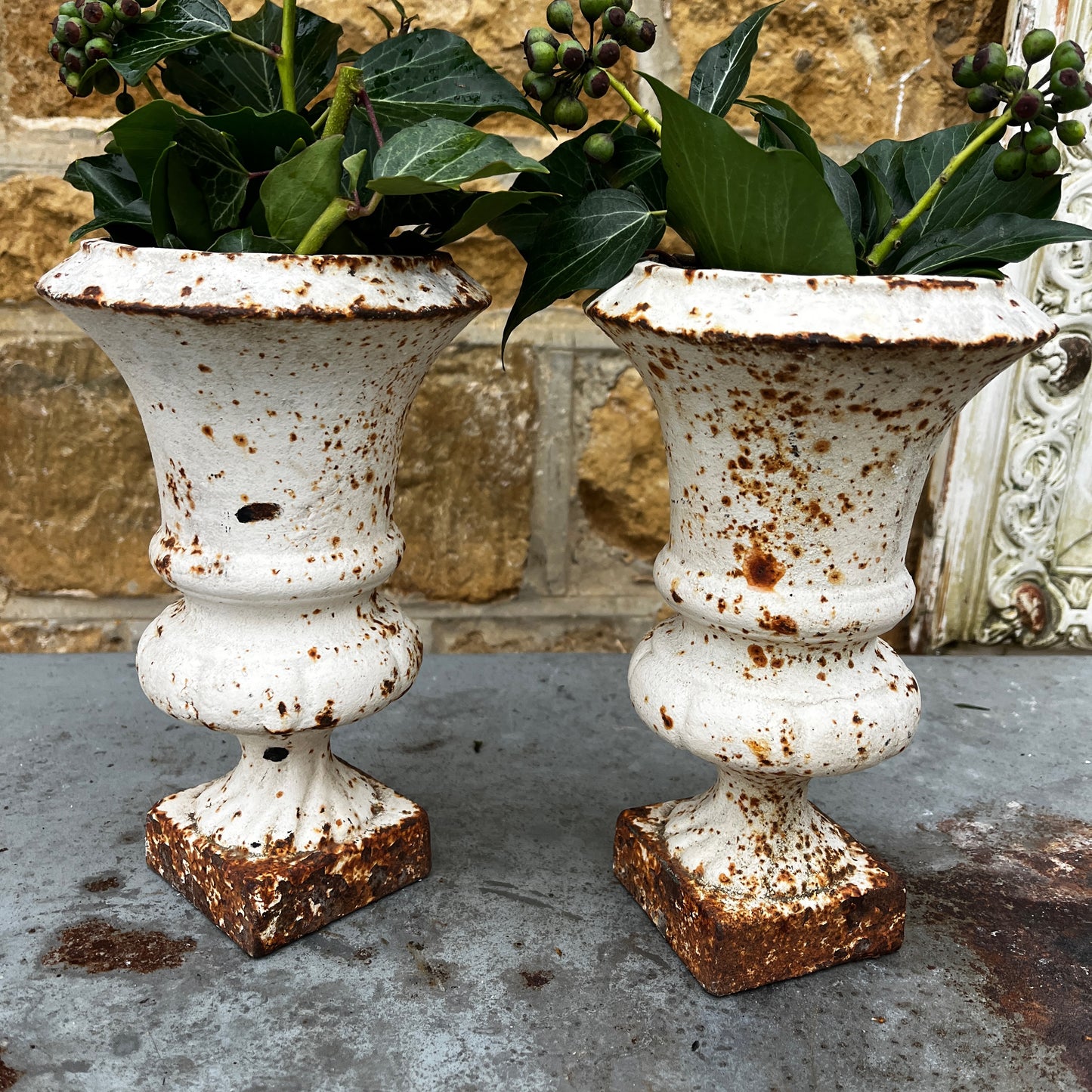 Pair of vintage Camana urns in a white finish. The urns feature classic shapes with decorative detailing and a weathered, aged patina, giving them a rustic, antique charm.