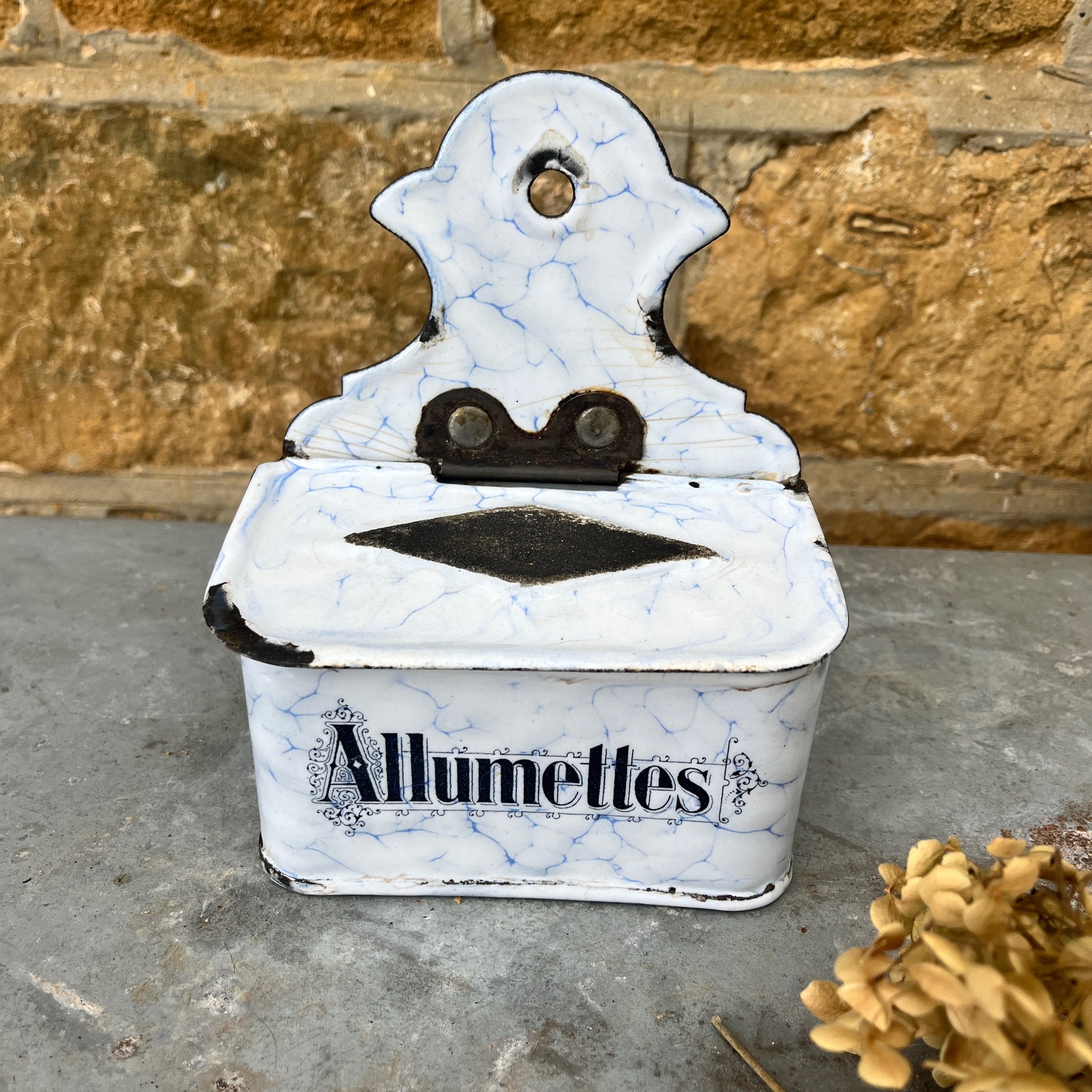 A vintage enamel allumettes box with a white background and blue hand-painted  geometric patterns, featuring a smooth, glossy finish. The small, rectangular box has a hinged lid, exuding classic French charm