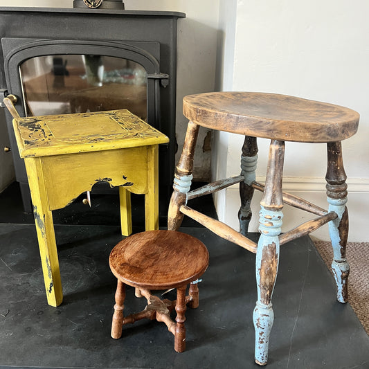 A collection of rustic wooden stools, each with a weathered finish in varying shades of brown, blue and yellow, featuring simple, sturdy designs with four legs