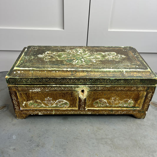 A vintage Florentine jewellery box with a rectangular shape, featuring a rich gold exterior with intricate green accents. The box is adorned with ornate, baroque-style gold detailing along the edges and corners, showcasing classic Florentine craftsmanship. The lid opens to reveal a luxurious red fabric lining.   The box stands on small gold coloured feet, exuding antique charm and sophistication.