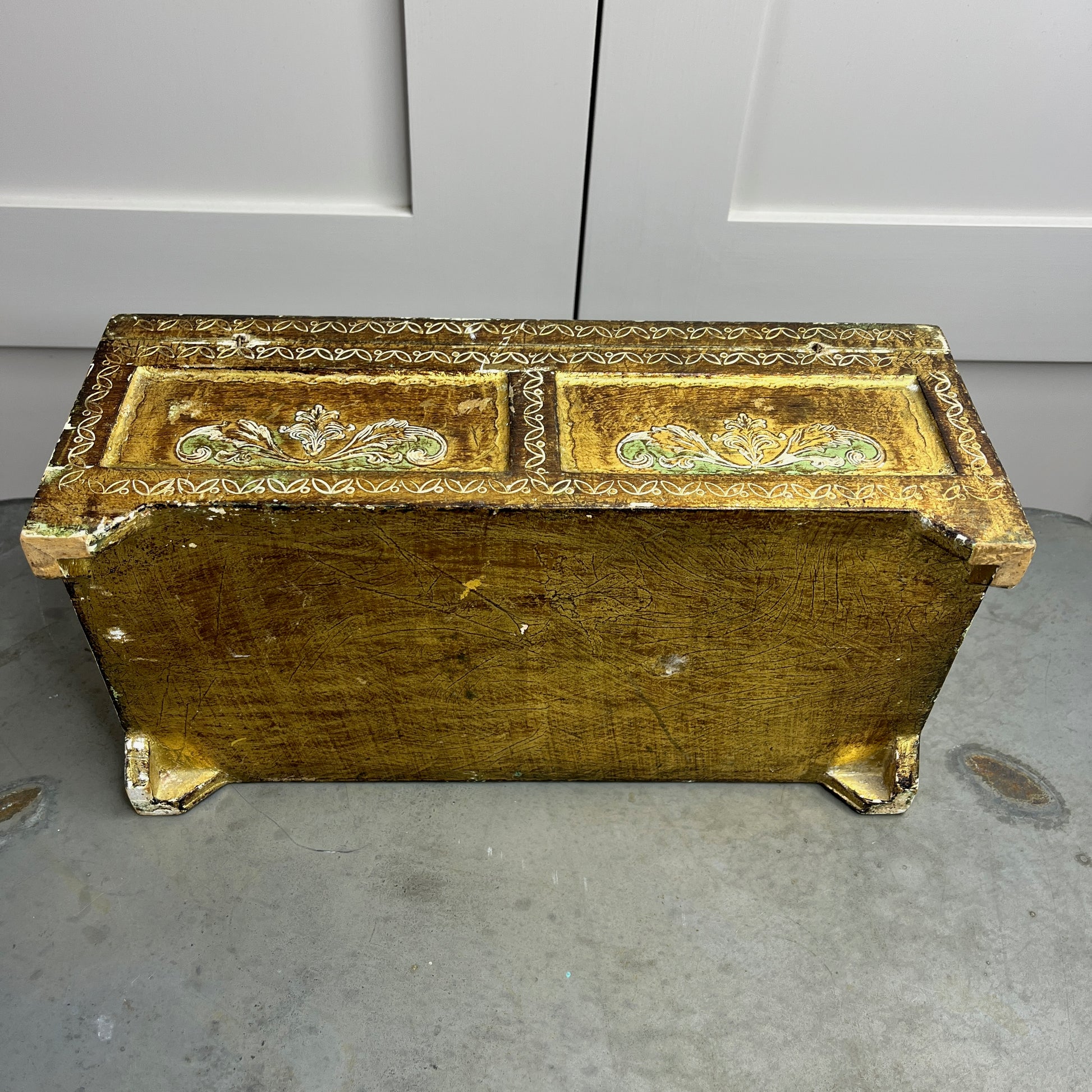 A vintage Florentine jewellery box with a rectangular shape, featuring a rich gold exterior with intricate green accents. The box is adorned with ornate, baroque-style gold detailing along the edges and corners, showcasing classic Florentine craftsmanship. The lid opens to reveal a luxurious red fabric lining.   The box stands on small gold coloured feet, exuding antique charm and sophistication.