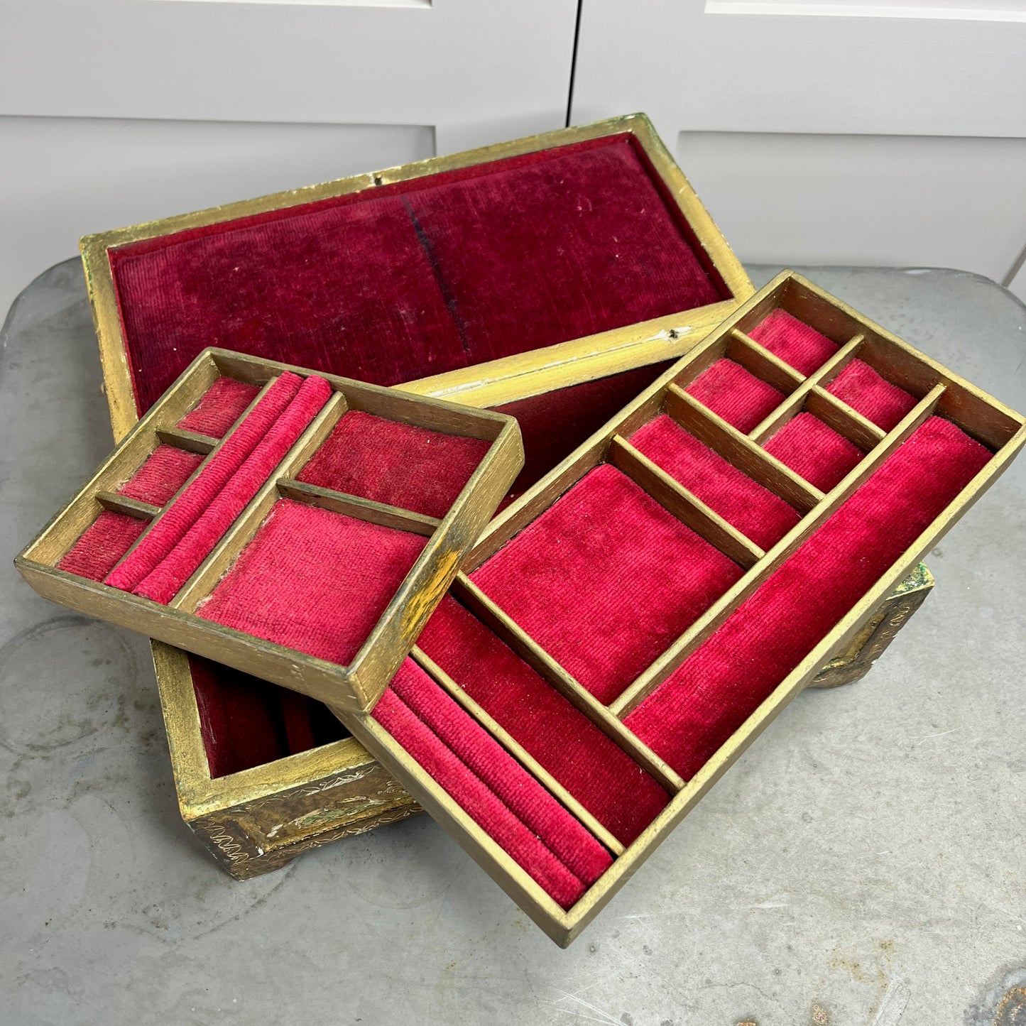 A vintage Florentine jewellery box with a rectangular shape, featuring a rich gold exterior with intricate green accents. The box is adorned with ornate, baroque-style gold detailing along the edges and corners, showcasing classic Florentine craftsmanship. The lid opens to reveal a luxurious red fabric lining.   The box stands on small gold coloured feet, exuding antique charm and sophistication.