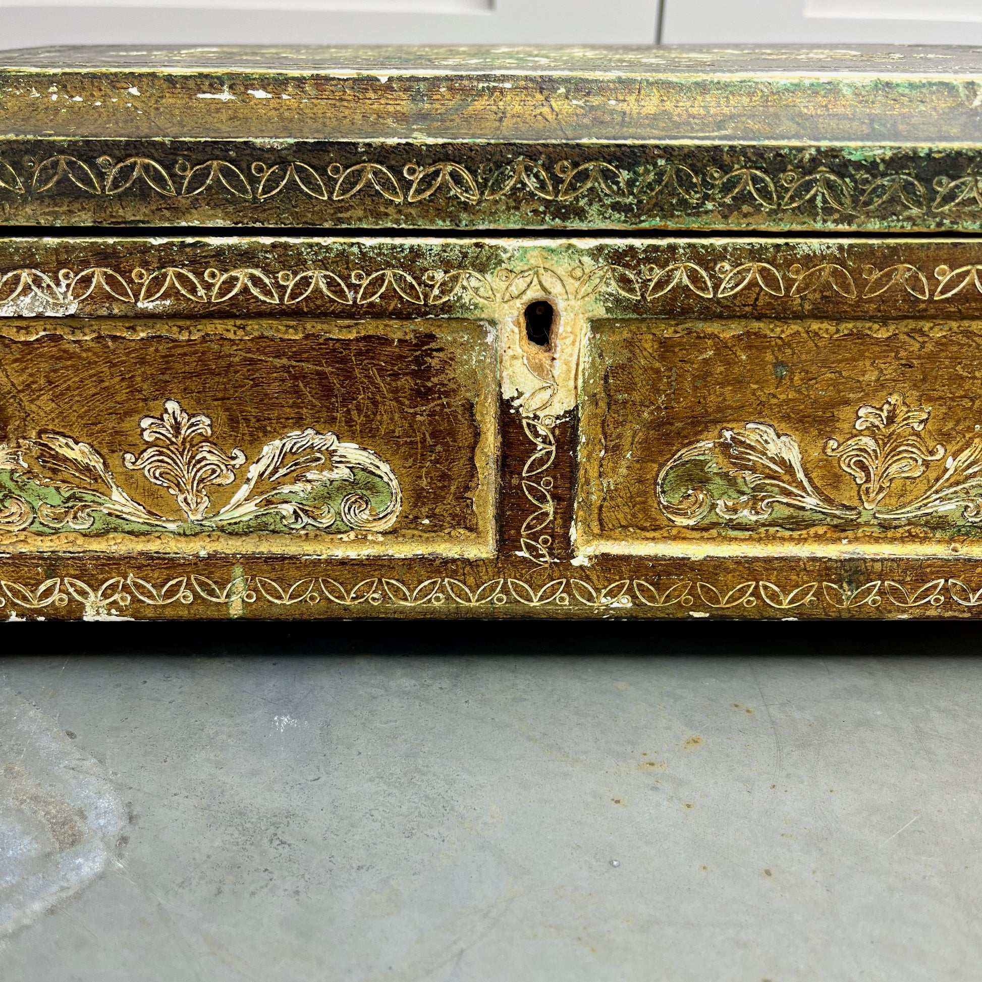 A vintage Florentine jewellery box with a rectangular shape, featuring a rich gold exterior with intricate green accents. The box is adorned with ornate, baroque-style gold detailing along the edges and corners, showcasing classic Florentine craftsmanship. The lid opens to reveal a luxurious red fabric lining.   The box stands on small gold coloured feet, exuding antique charm and sophistication.