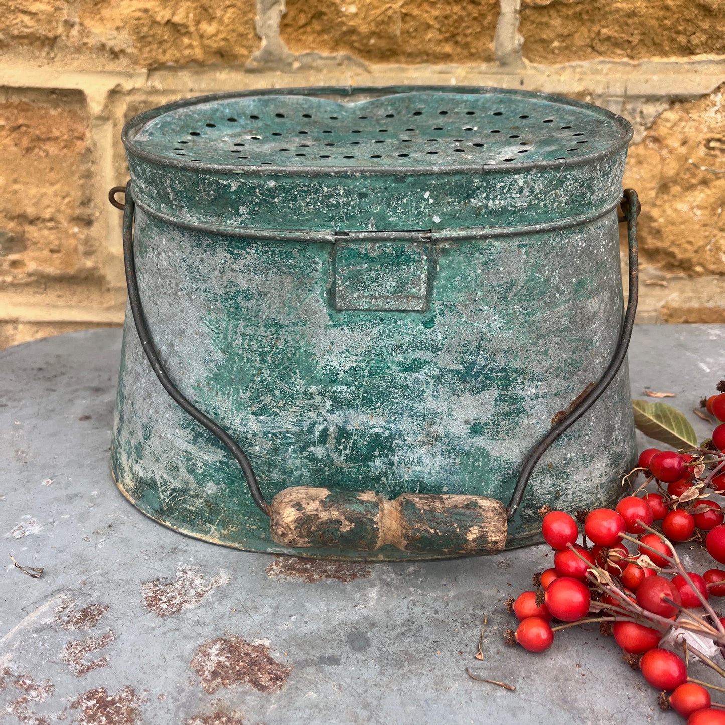 Vintage green metal container with red berries on a stone surface