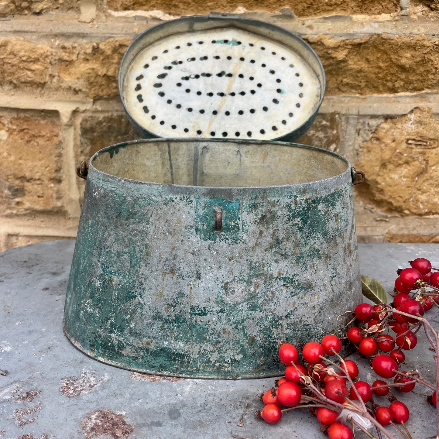 Vintage metal bait pot with red berries on a stone surface