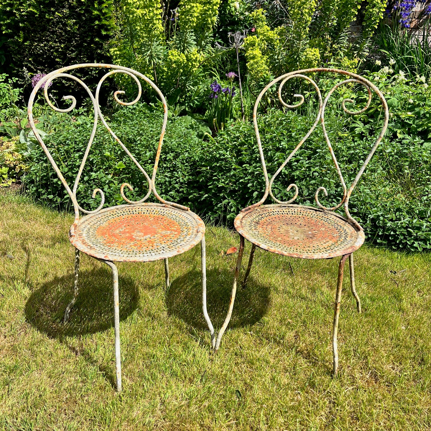 A French vintage bistro set featuring a round table with a green and orange weathered finish, paired with matching chairs that show a distressed, rustic texture. The set exudes classic outdoor charm, with the table’s smooth surface and the chairs’ slightly worn frames