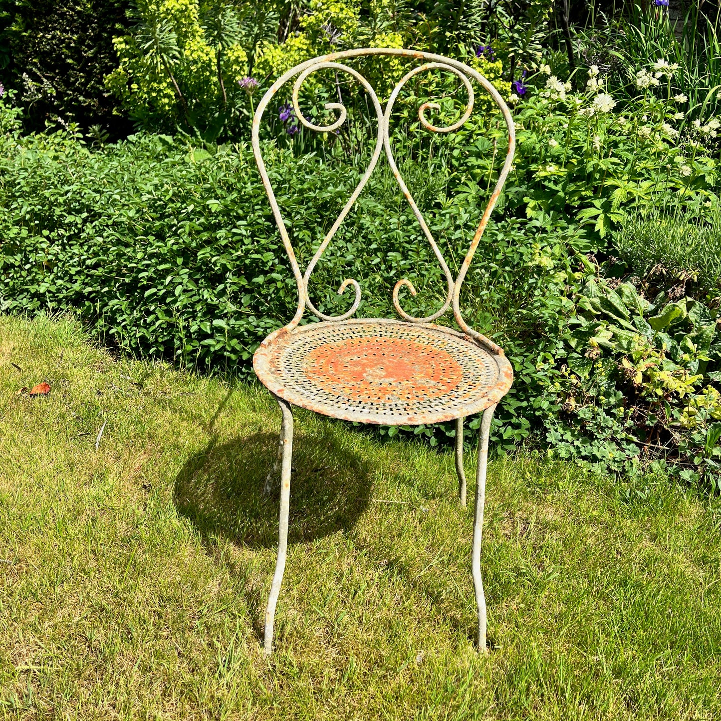 A French vintage bistro set featuring a round table with a green and orange weathered finish, paired with matching chairs that show a distressed, rustic texture. The set exudes classic outdoor charm, with the table’s smooth surface and the chairs’ slightly worn frames
