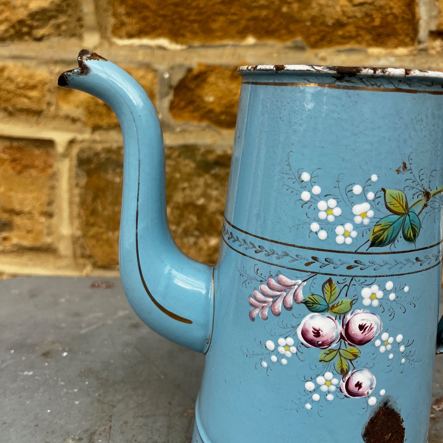 A vintage French enamel jug with a charming floral pattern in soft pink, green, and white tones on a light blue enamel background.