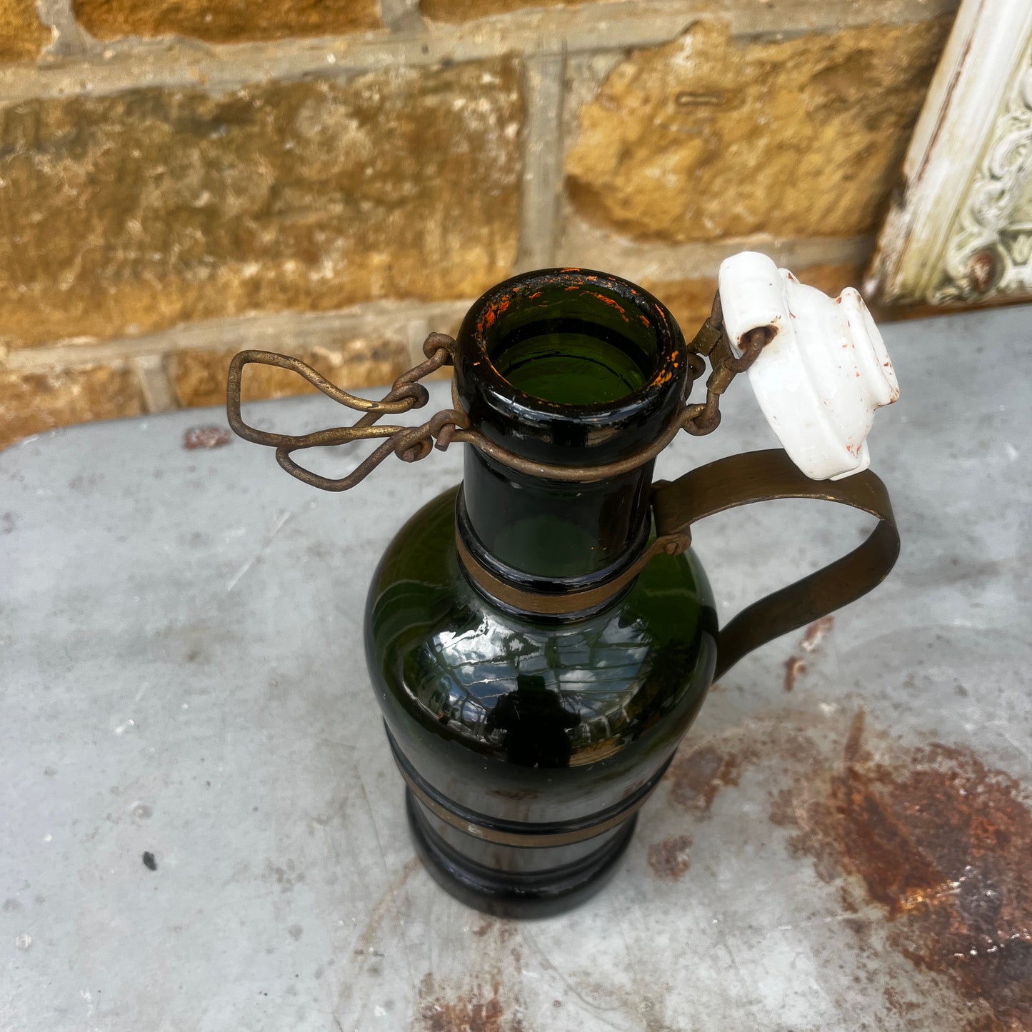 An antique French green glass bottle with a rounded body, ceramic swing-top stopper, and aged metal carry handle