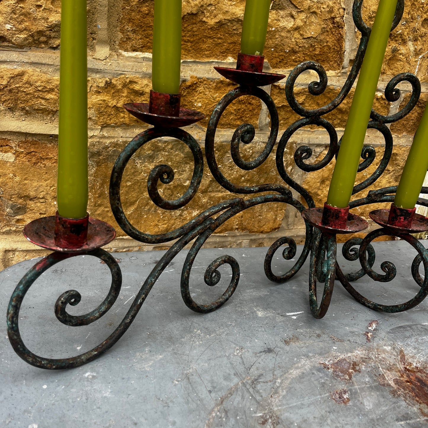 Decorative candle holder with green candles against a stone wall.