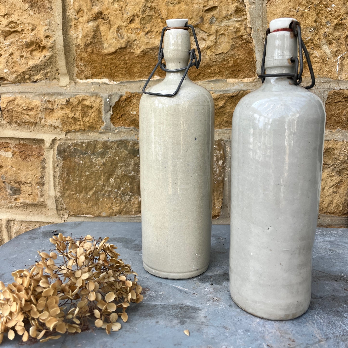A pair of French stone bottles crafted from durable ceramic with a rustic, glazed finish, each featuring a hinged lid with a metal clasp.