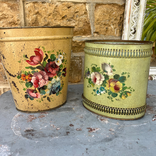 A pair of French tole peinte waste bins, hand-painted with intricate floral designs in soft pastels on a green or mustard background.
