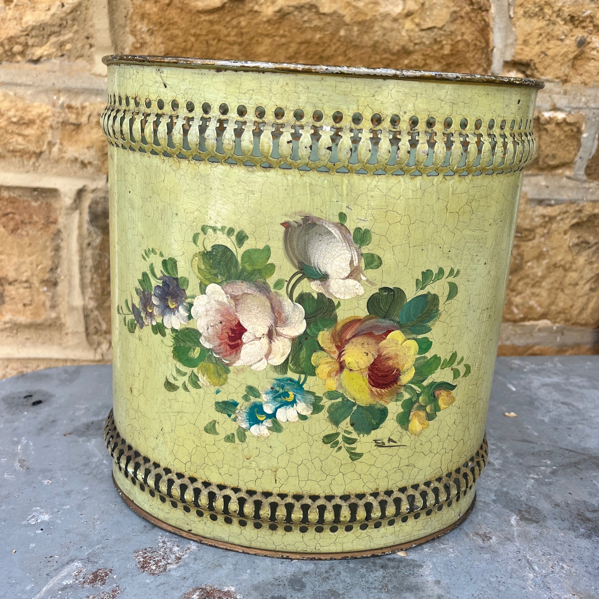 A pair of French tole peinte waste bins, hand-painted with intricate floral designs in soft pastels on a green or mustard background.
