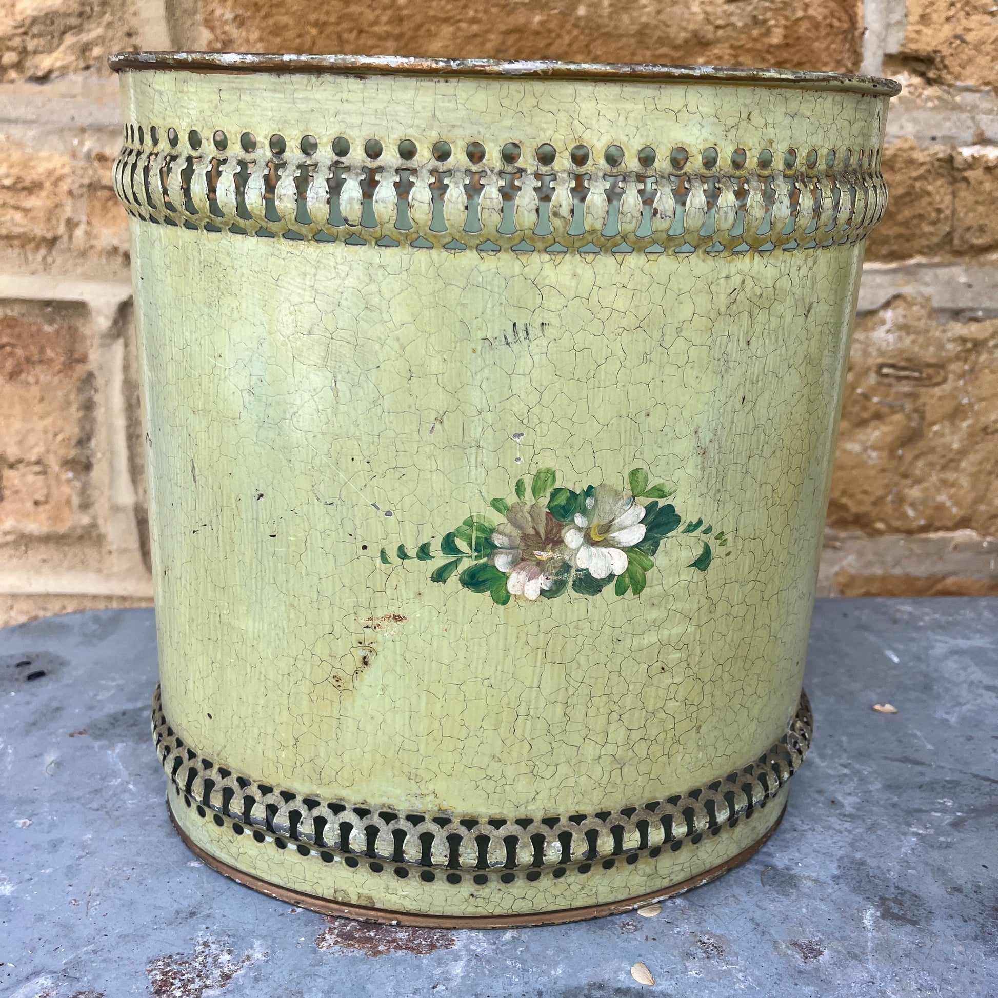 A pair of French tole peinte waste bins, hand-painted with intricate floral designs in soft pastels on a green or mustard background.