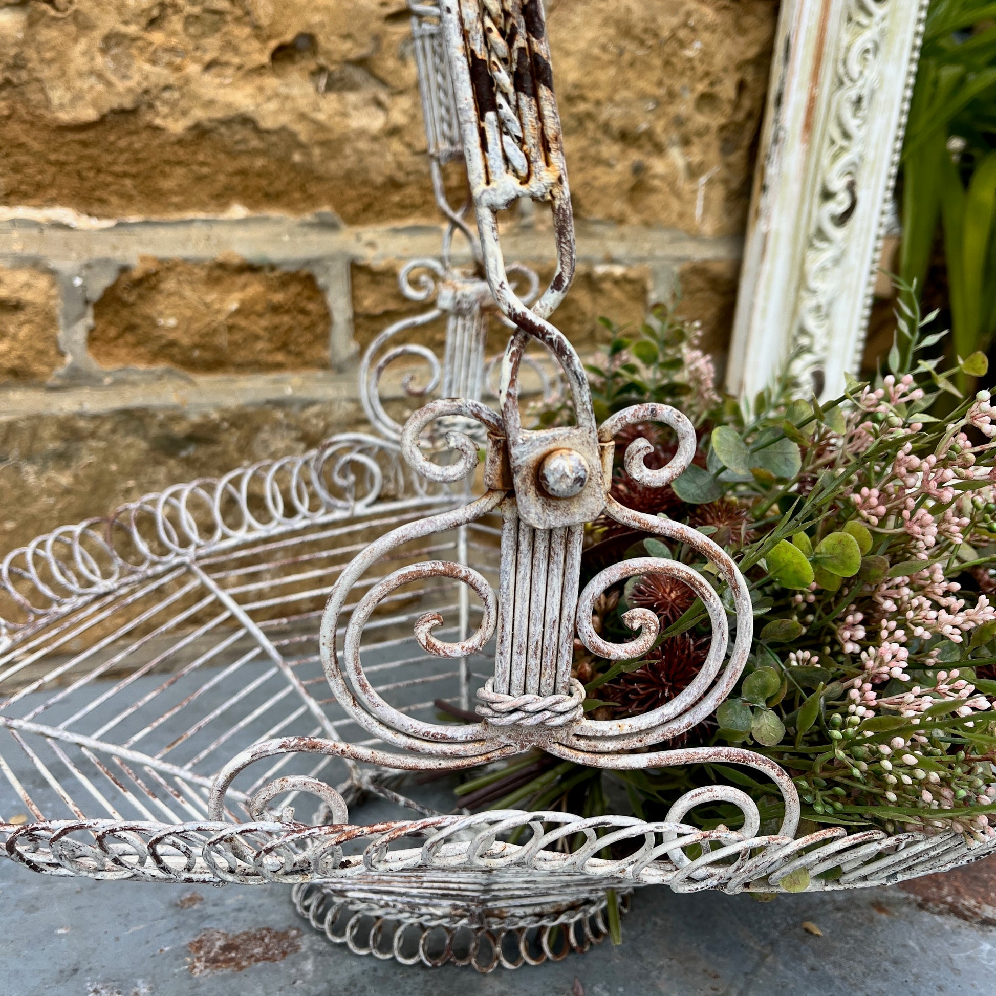 A French wire basket with a white, weathered finish, featuring an open, lattice-like design with delicate, curved edges. The basket includes one sturdy hinged handle, exuding rustic charm