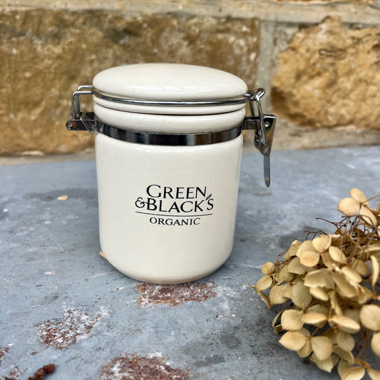 A ceramic jar,  with a hinged lid featuring a classic design, labeled Green & Black's organic. The jar has a vintage, sturdy look.