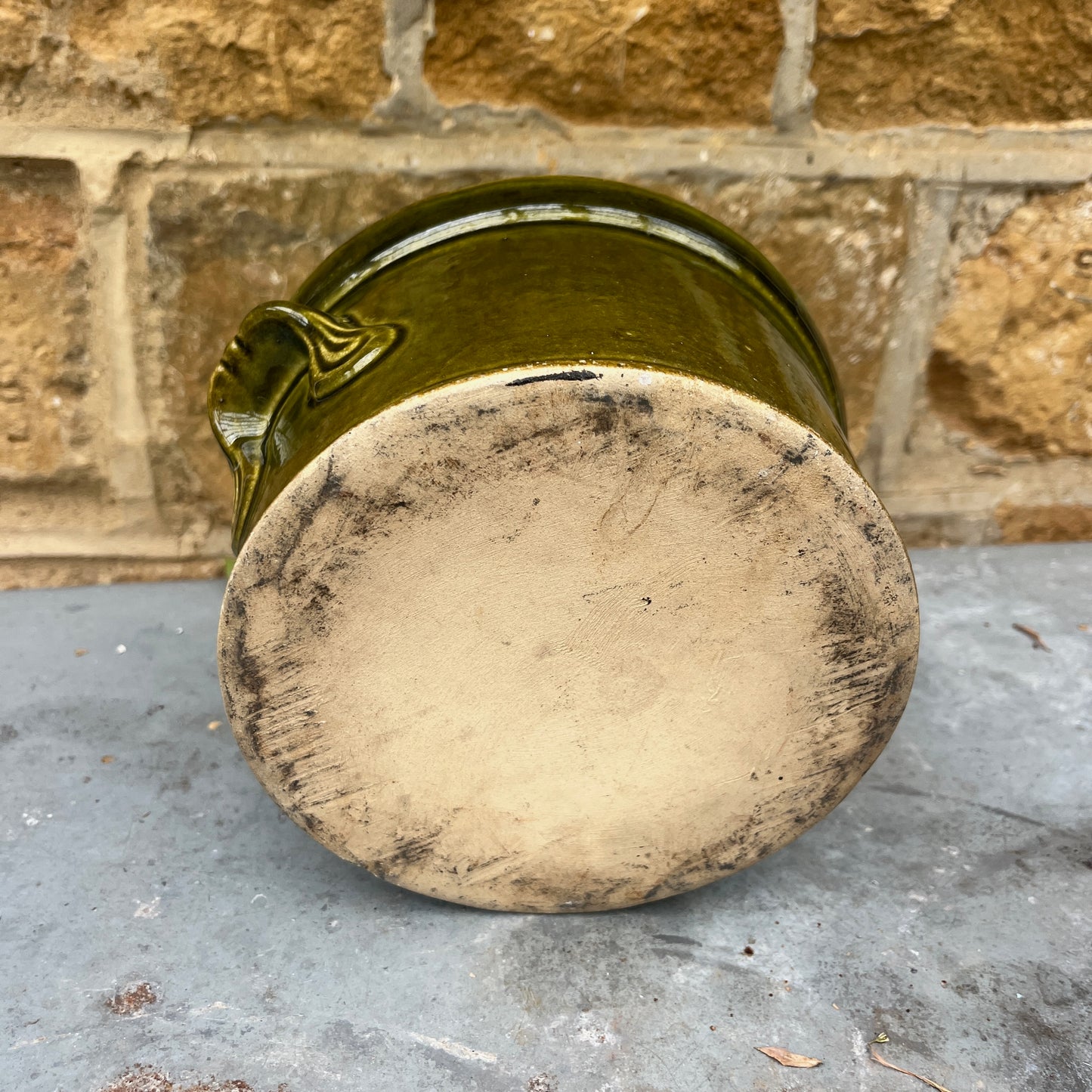 Green ceramic pot with a textured base on a stone surface