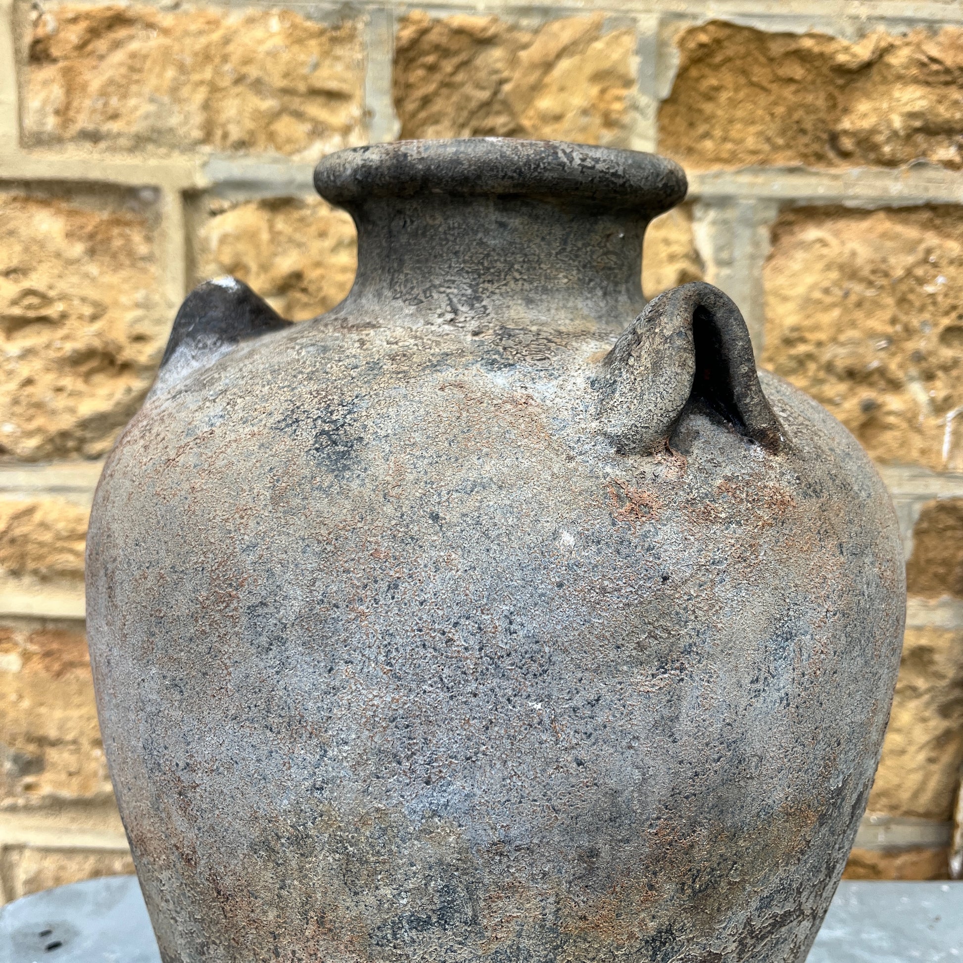 A large ceramic pot with a textured brown & black finish, featuring three evenly spaced handles around its wide, rounded body. The pot has a rough, slightly textured surface, exuding modern elegance
