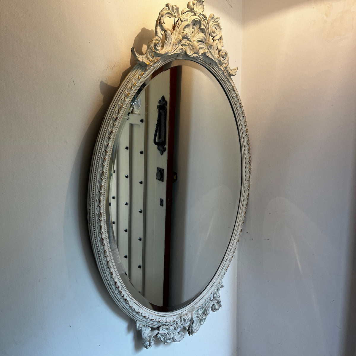 Large vintage French oval bevelled mirror painted white, featuring decorative detailing at the top and bottom with an elegant aged finish.