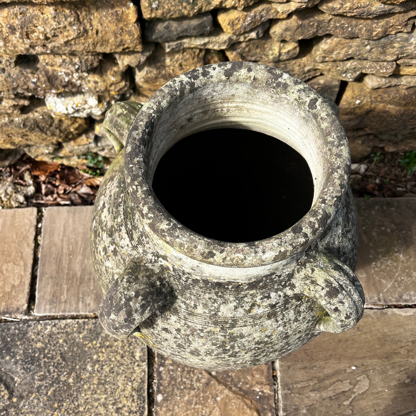 Large rustic garden urn with an aged weathered surface and traces of green lichen, featuring a classic decorative shape and timeworn outdoor character.
