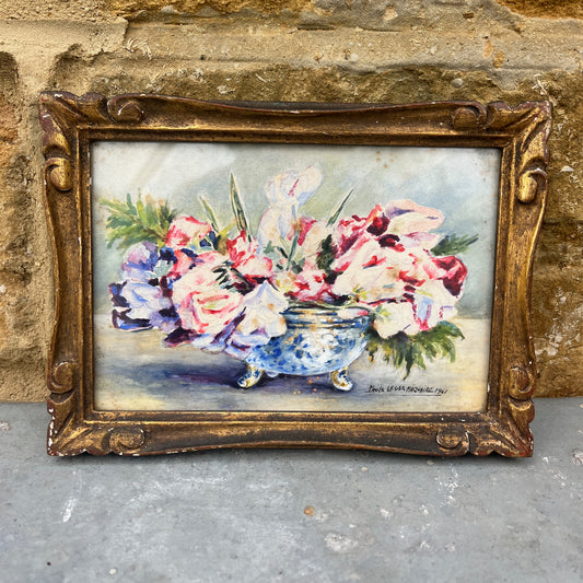 Vintage painting of flowers in a bowl with a gold frame against a textured wall.