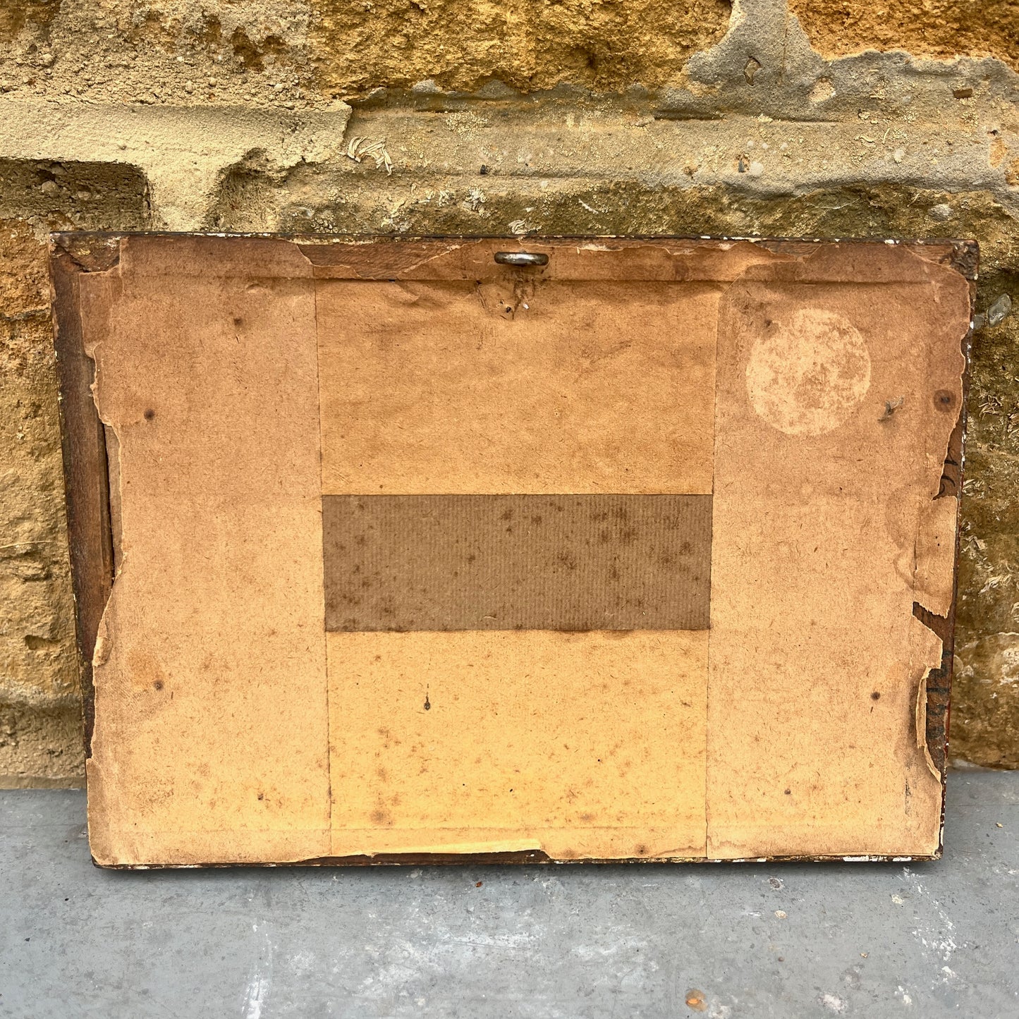 Back of an old painting with visible wear against a stone wall.