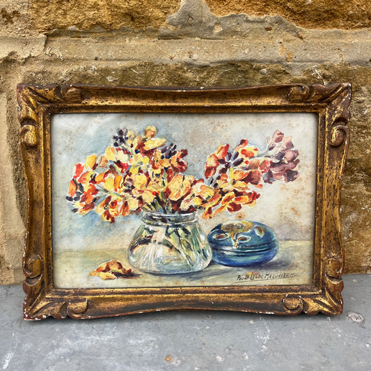 Vintage painting of flowers in a vase with a gold frame against a textured stone wall.