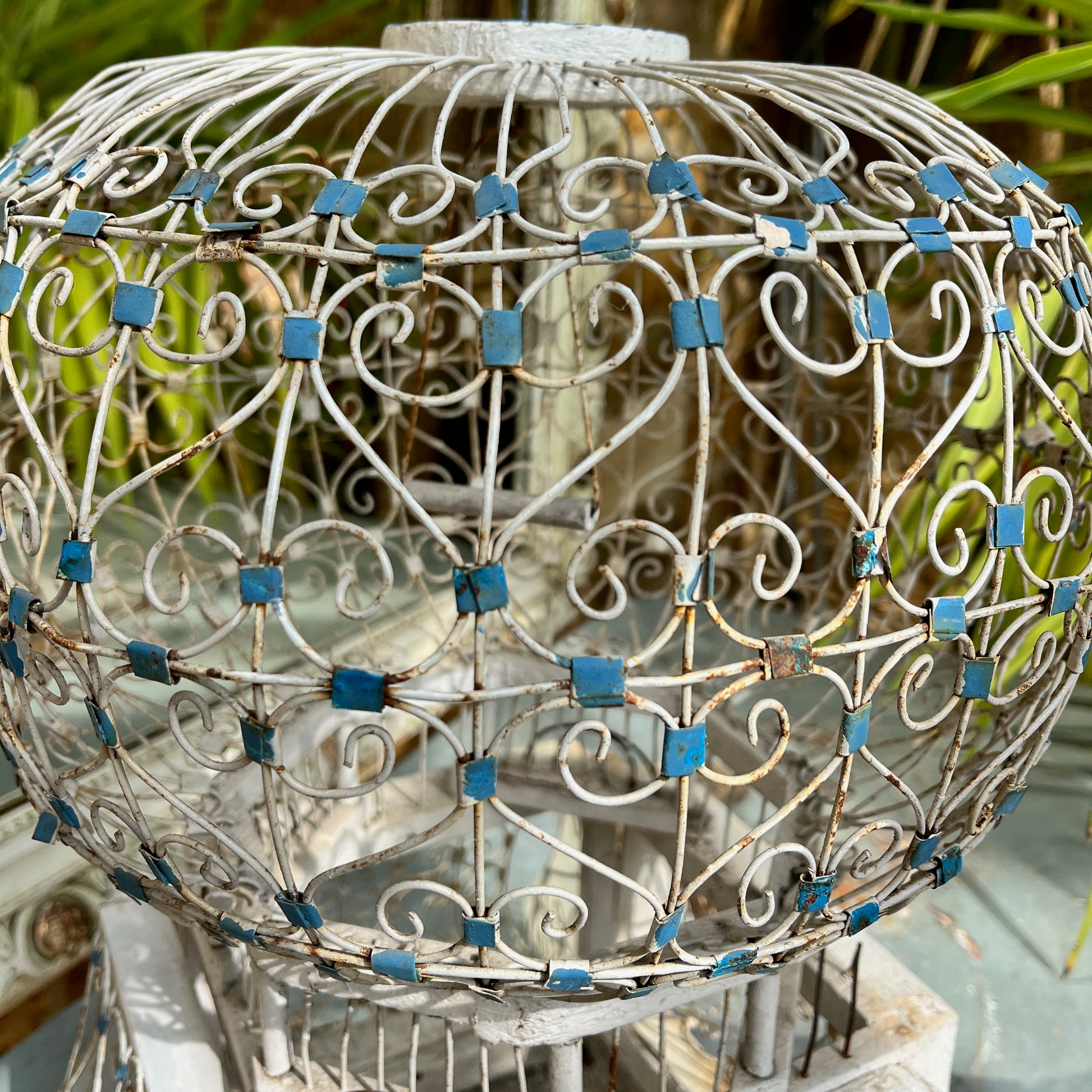 A Moroccan-style bird cage painted in blue and white, featuring intricate geometric and arabesque patterns. The cage has a domed top with a small finial, crafted from lightweight metal with open latticework, exuding exotic charm