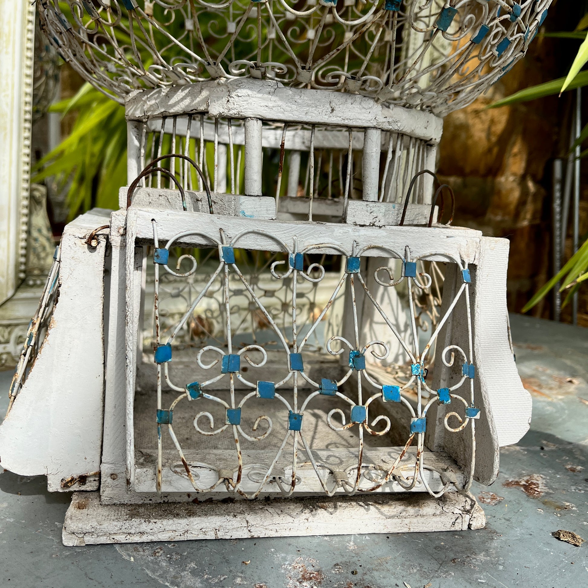 A Moroccan-style bird cage painted in blue and white, featuring intricate geometric and arabesque patterns. The cage has a domed top with a small finial, crafted from lightweight metal with open latticework, exuding exotic charm