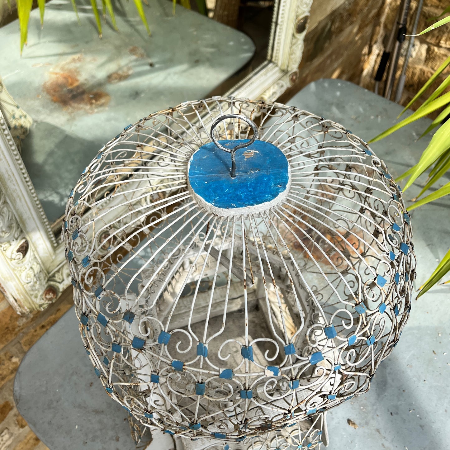 A Moroccan-style bird cage painted in blue and white, featuring intricate geometric and arabesque patterns. The cage has a domed top with a small finial, crafted from lightweight metal with open latticework, exuding exotic charm