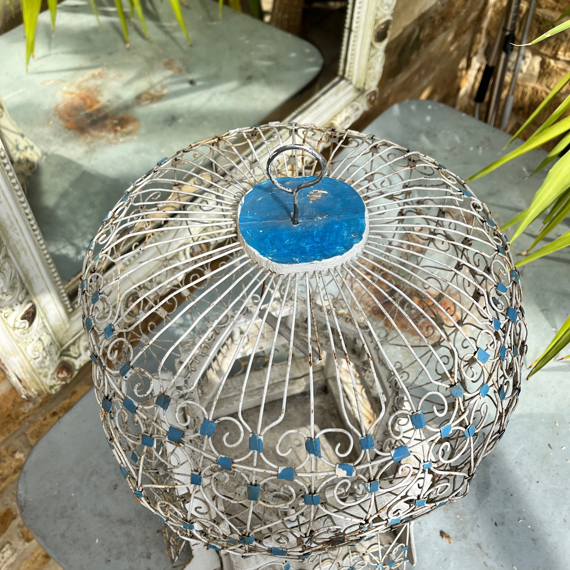 A Moroccan-style bird cage painted in blue and white, featuring intricate geometric and arabesque patterns. The cage has a domed top with a small finial, crafted from lightweight metal with open latticework, exuding exotic charm