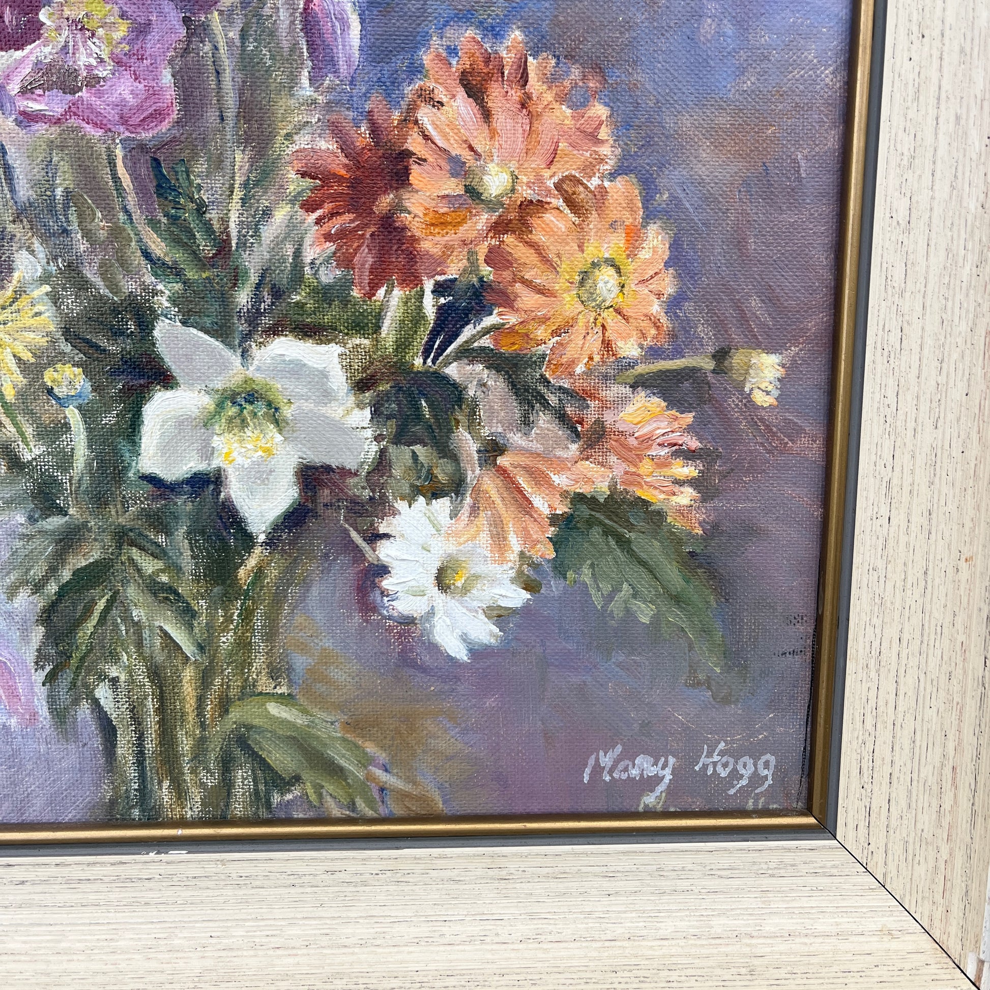 An oil on canvas painting by Mary Hogg, showcasing a vibrant arrangement of flowers with bold brushstrokes in shades of purple, yellow, orange and green. The floral composition, set against a soft, blurred background, exudes a lively, impressionistic charm