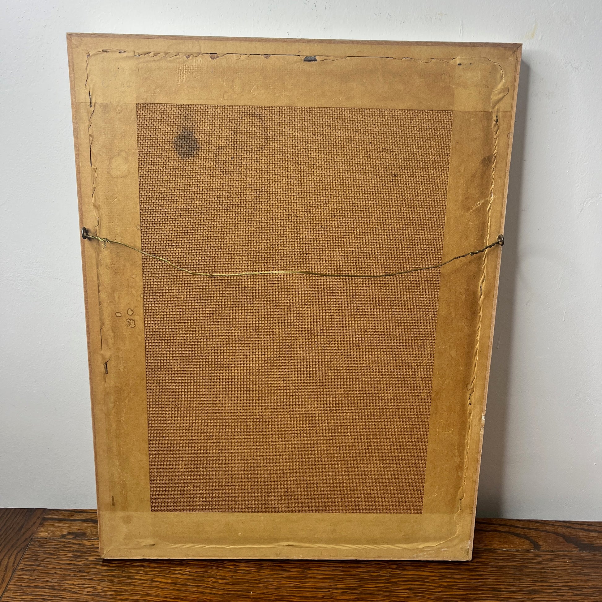 Back of an old painting with a textured brown surface on a white wall.