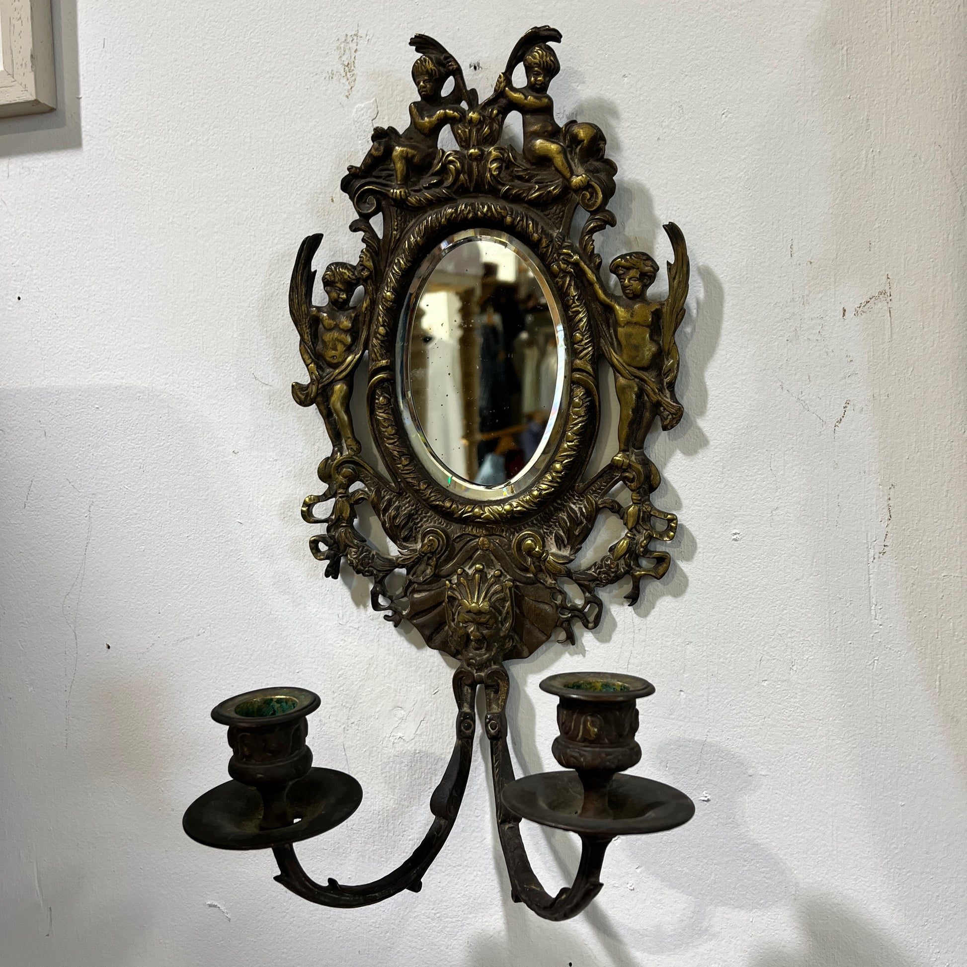 Elegant pair of antique French cenelle sconces featuring intricate scrollwork and a weathered patina and bevelled oval mirror, reflecting classic 19th-century craftsmanship.