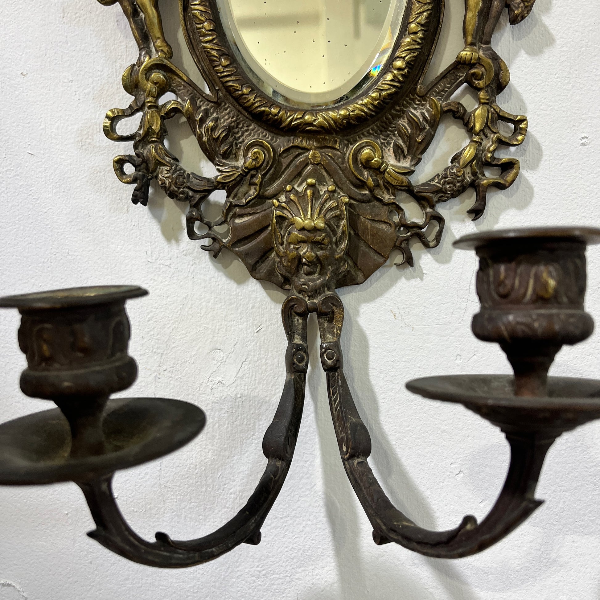 Elegant pair of antique French cenelle sconces featuring intricate scrollwork and a weathered patina and bevelled oval mirror, reflecting classic 19th-century craftsmanship.