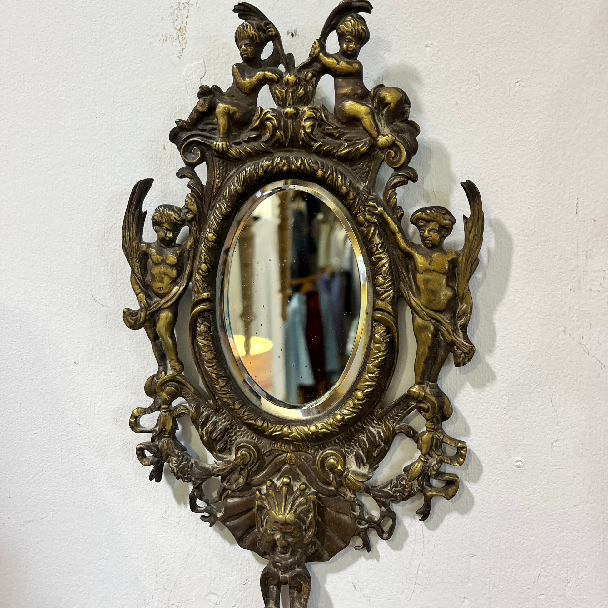 Elegant pair of antique French cenelle sconces featuring intricate scrollwork and a weathered patina and bevelled oval mirror, reflecting classic 19th-century craftsmanship.