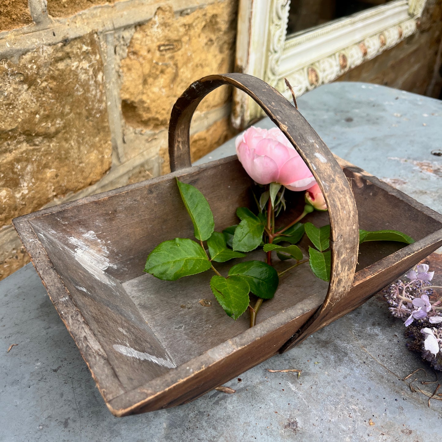 Vintage-style wooden basket with pink flower and green leaves on a stone surface.
