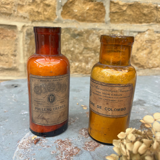 A pair of antique spice or medicine jars made of brown glass, each featuring etched labels and cork stoppers, filled with contents such as dried herbs and powders. The jars have a vintage, apothecary-style design.