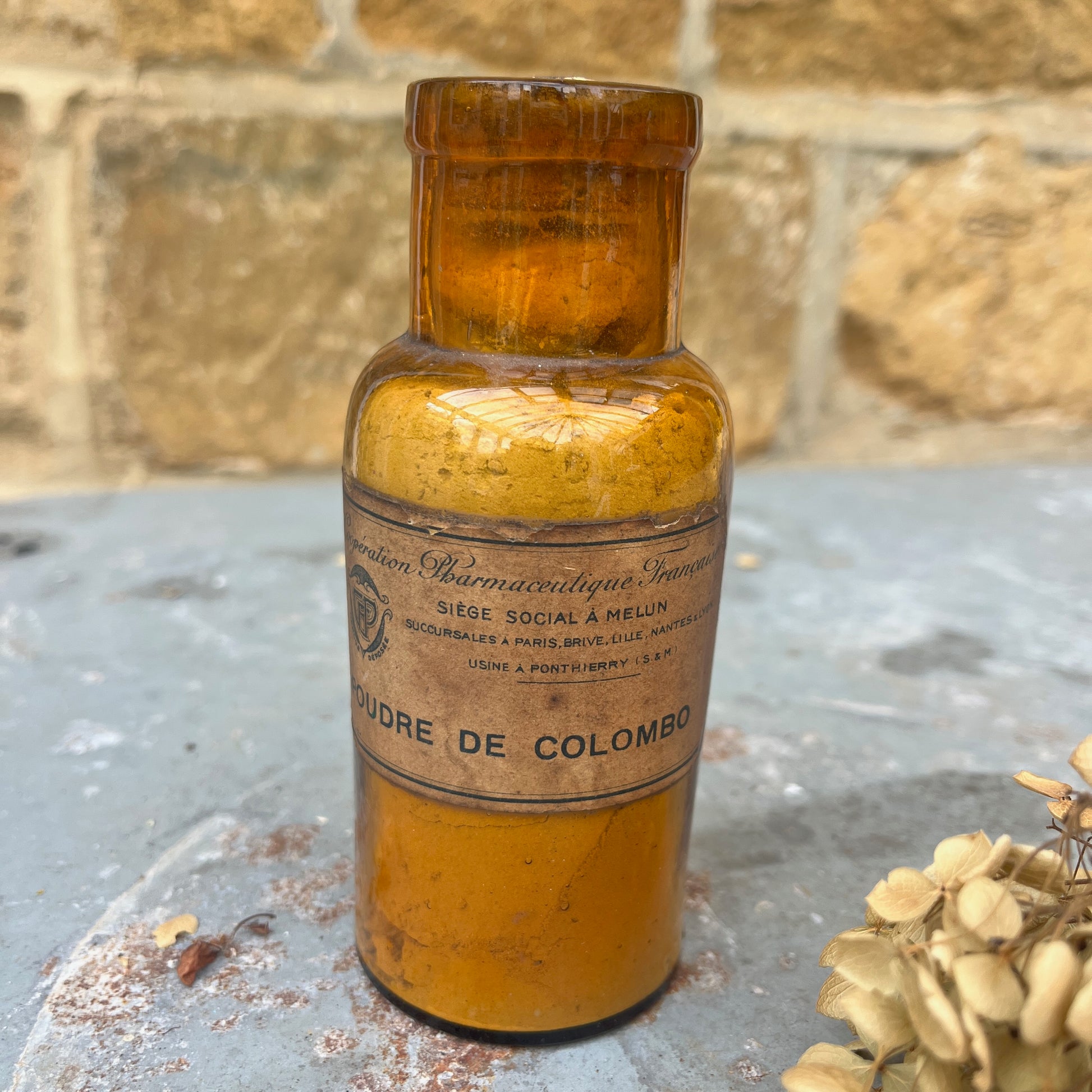 A pair of antique spice or medicine jars made of brown glass, each featuring etched labels and cork stoppers, filled with contents such as dried herbs and powders. The jars have a vintage, apothecary-style design.