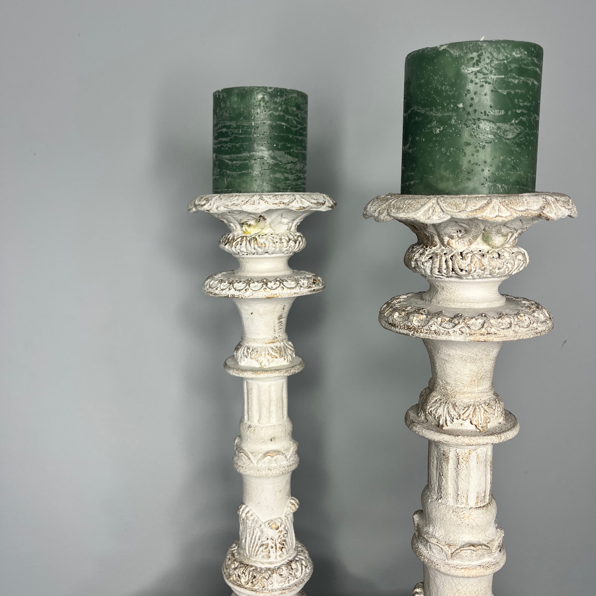 A pair of tall French-style candle holders crafted from wood, painted white, featuring elegant, carved detailing and a slightly distressed finish. Each holder supports a single candle, exuding classic rustic charm
