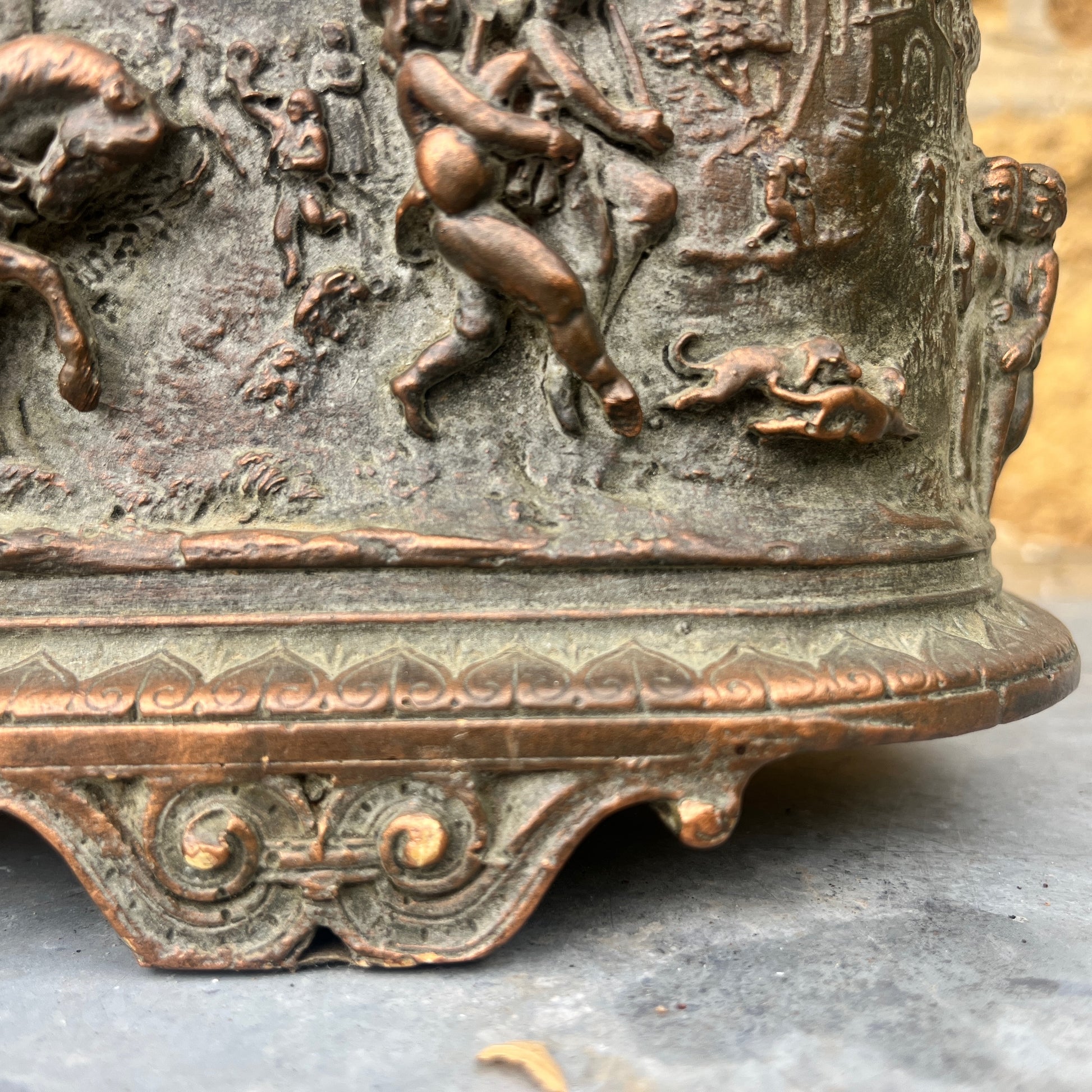 A vintage terracotta jardinière with a rich, earthy finish, featuring an intricately moulded frieze scene of classical figures and animals encircling its exterior. The cylindrical planter has a slightly weathered texture, exuding rustic elegance