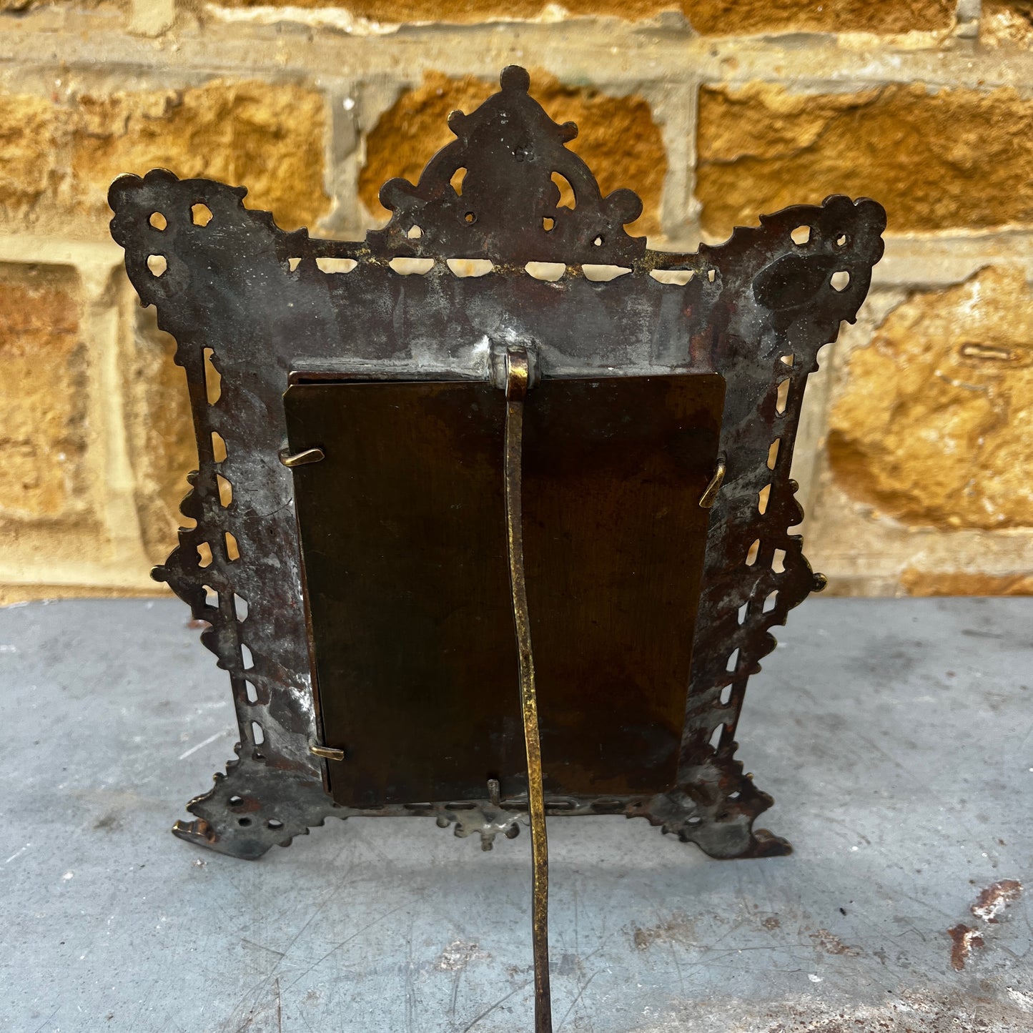 An ornate antique gilt metal photo frame with intricate pierced scrollwork, floral motifs, and a richly aged gold finish. The rectangular frame stands on decorative feet with an elaborate crest at the top, showcasing exceptional Victorian-era craftsmanship