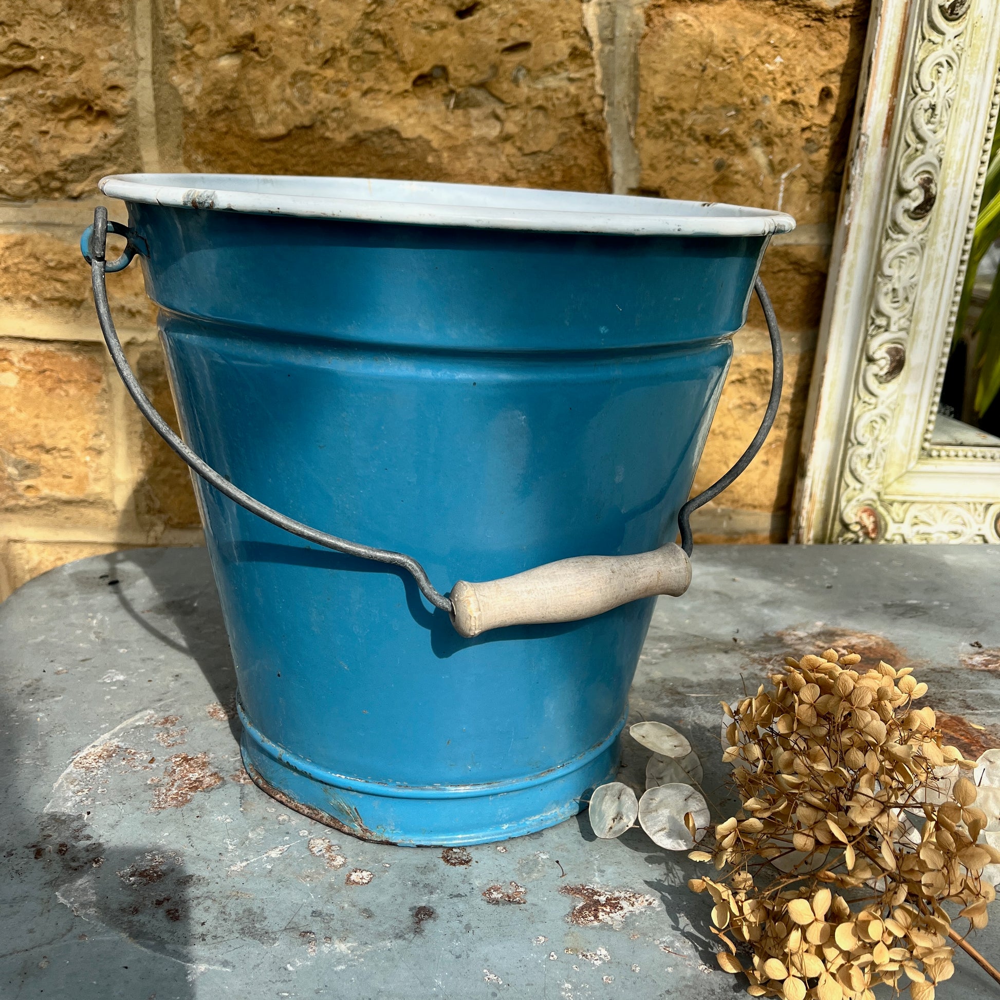 Vintage-style blue metal bucket with white enamel interior and wooden grip handle, placed on a rustic surface