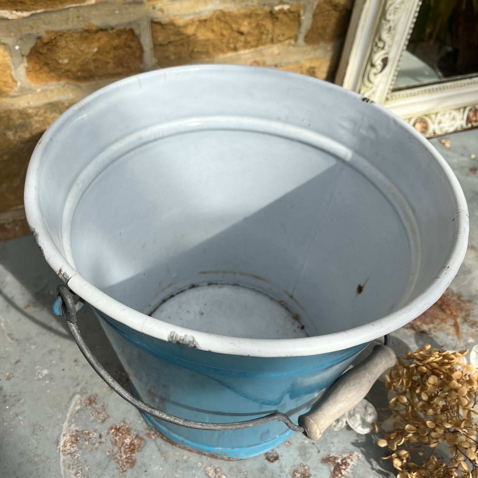 Vintage-style blue metal bucket with white enamel interior and wooden grip handle, placed on a rustic surface
